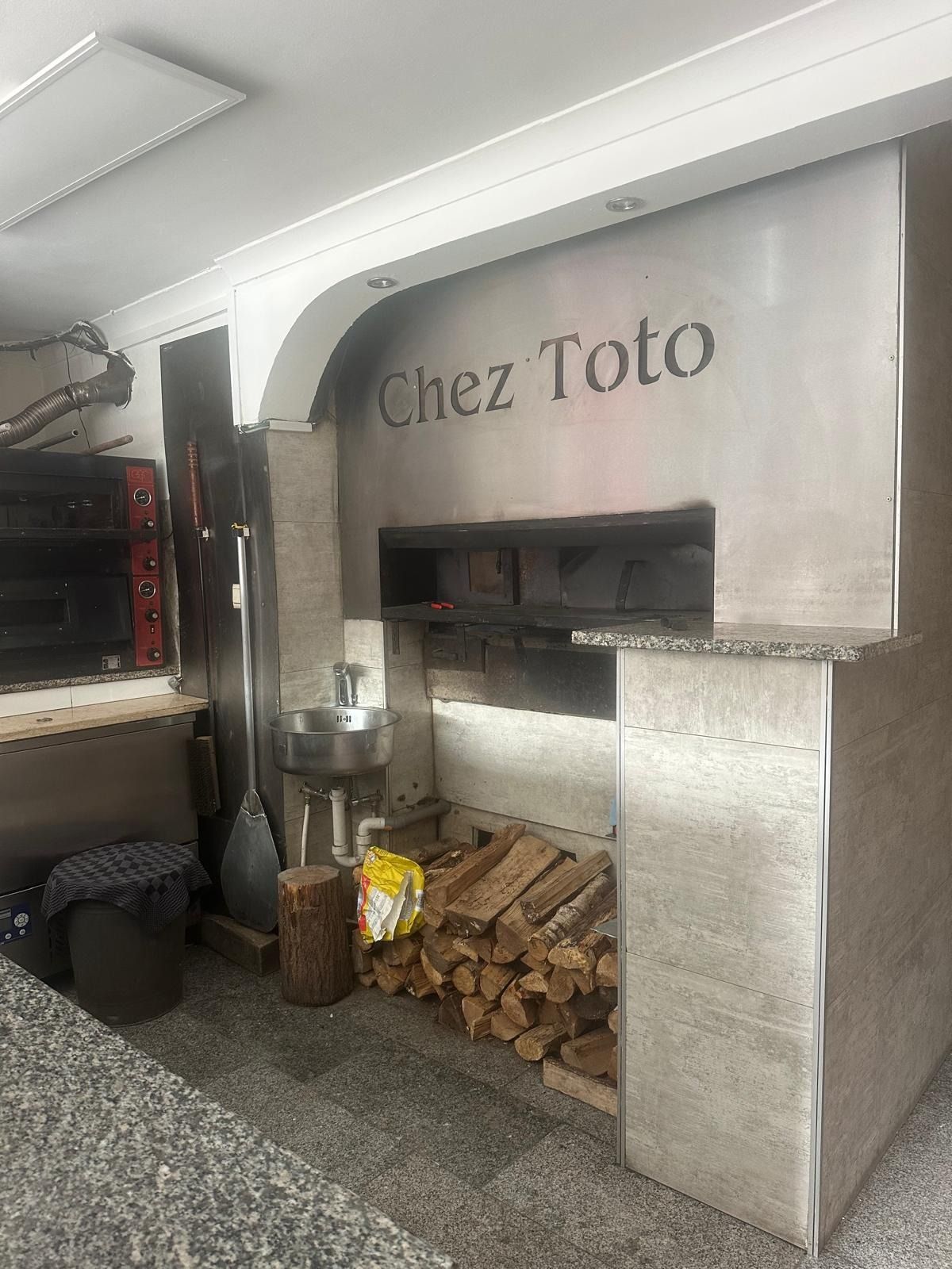 Le four à bois de Chez Toto, avec son nom gravé et la réserve de bûches
